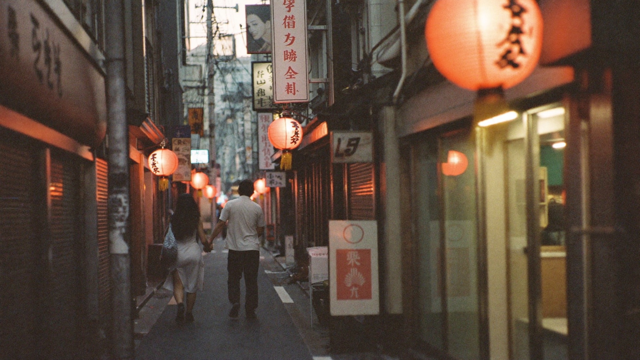 A couple walking hand in hand down a lantern-lit Tokyo alley
