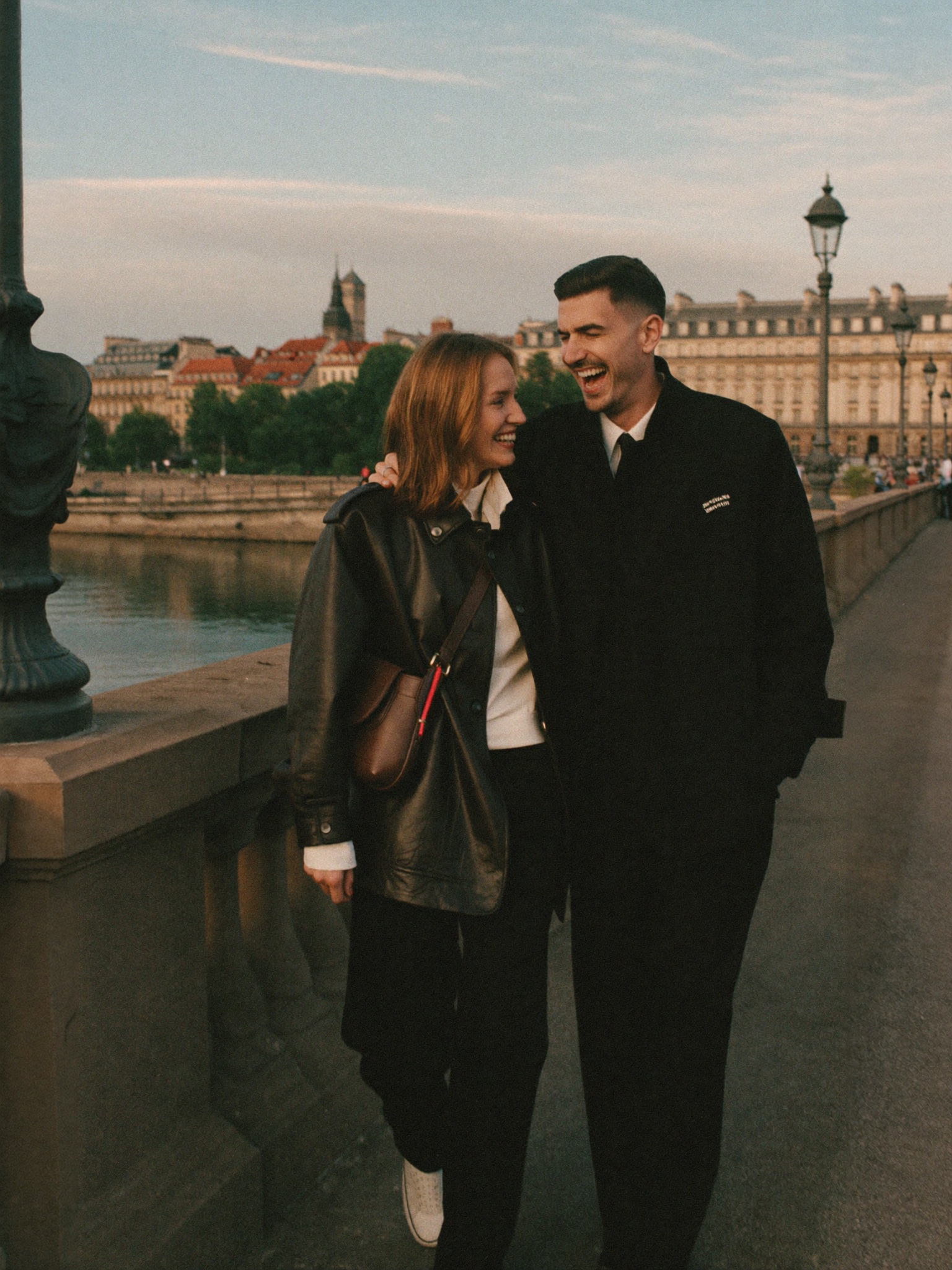 A couple walking a river bridge at golden hour, laughing