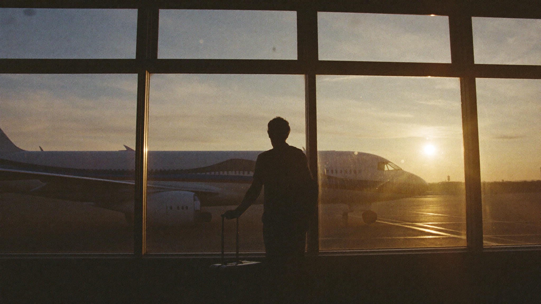 A traveller silhouetted at an airport window at sunrise