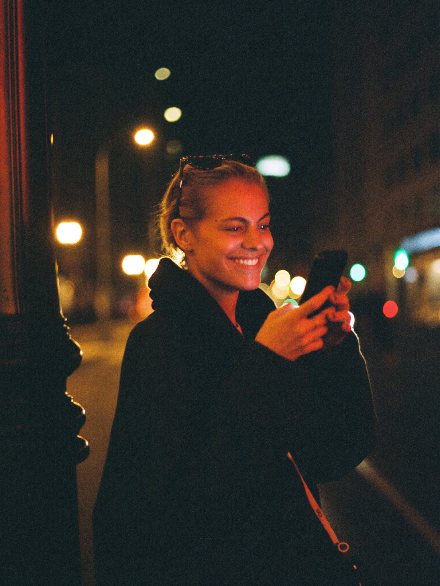 A woman smiling at her phone on a neon-lit street at night